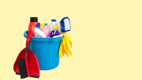 Cleaning supplies in blue bucket on pastel yellow background — Stock Photo, Image