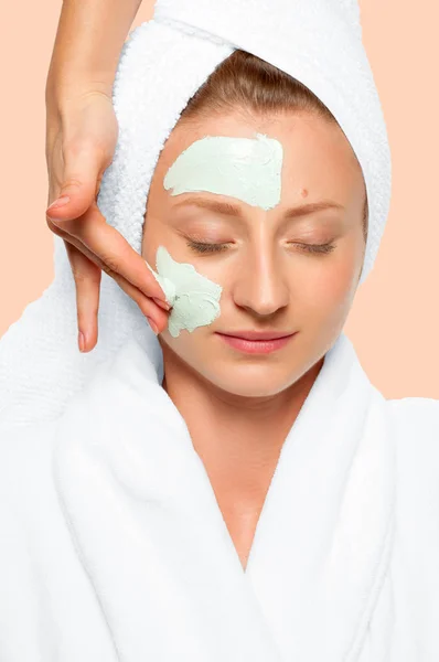 Beauty Spa. Woman applying clay mask on face. Pastel background — Stock Photo, Image