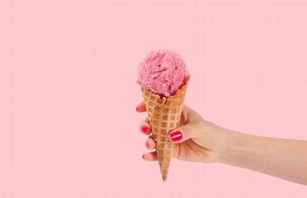 Hand hält Erdbeer-Eiskegel auf rosa verblasstem Pastell-Hintergrund. — Stockfoto