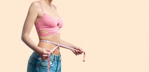 Mulher está medindo a cintura após a perda de peso no fundo pastel desbotada — Fotografia de Stock