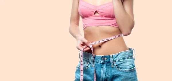 Woman is measuring waist after weight loss on faded pastel background — Stock Photo, Image