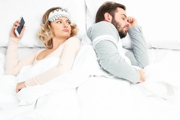 Mujer joven usando teléfono inteligente mientras su marido está durmiendo — Foto de Stock