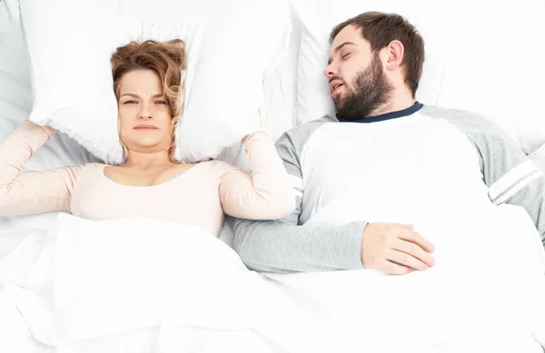 Man snoring and woman can't sleep, covering ears with pillow for snore noise — Stock Photo, Image