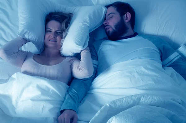 Hombre roncando y mujer no puede dormir, cubriendo oídos con almohada para roncar ruido — Foto de Stock