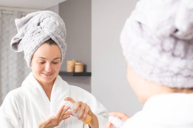 Güzel genç bir kadın yüzüne nemlendirici sürüyor..