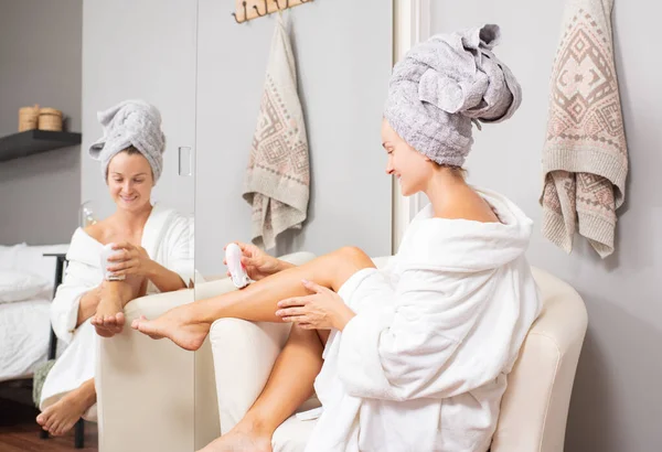 Woman is removing hair on her leg with an delectric epilator at home. — Stock Photo, Image