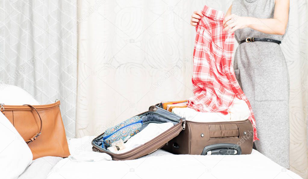 Beautiful woman packing suitcase in bedroom getting ready for road trip.