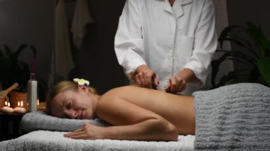Güzel, genç bir kadın masaj salonundan sıcak taşlar alıyor. Masör masaj masasında kadınlara profesyonel masaj yapıyor..