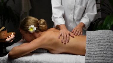 Kapalı gözlü güzel bir kadın masaj salonunda sırt masajı yaptırıyor. Masör masaj masasındaki kadına profesyonel masaj yapıyor..
