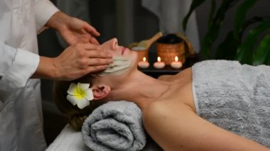 Kozmetik uzmanı kadın yüzüne kilden maske takıyor. Kadın güzellik merkezinde güzellik tedavisi görüyor..