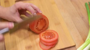 Dişi eller domatesi keser. Mutfak bıçağı kullanan kadın tahtada taze domates dilimliyor.
