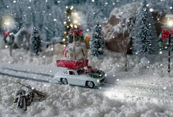 Miniaturní klasické auto nesoucí vánoční dárky na zasněžené zimní krajině — Stock fotografie