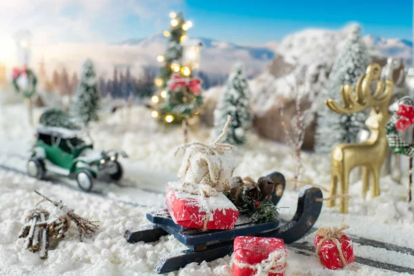 Schlitten beladen mit Geschenken und Miniatur-Auto, das einen Weihnachtsbaum durch verschneite Landschaft trägt — Stockfoto