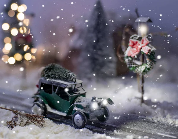 Miniaturní klasické auto nesoucí vánoční strom na zimním magickém pozadí — Stock fotografie