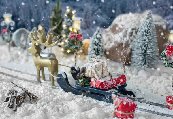 Schlitten beladen mit Geschenken und Miniatur-Auto, das einen Weihnachtsbaum durch verschneite Landschaft trägt — Stockfoto