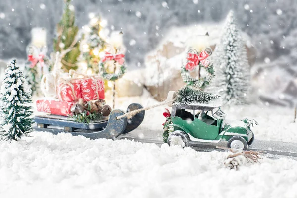 Miniaturní klasické auto nesoucí vánoční stromek a dárky na zasněžené silnici v zimě pozadí — Stock fotografie
