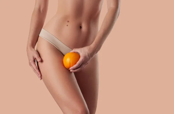 Slim woman is holding orange. Perfect female hips in underwear w — Stock Photo, Image