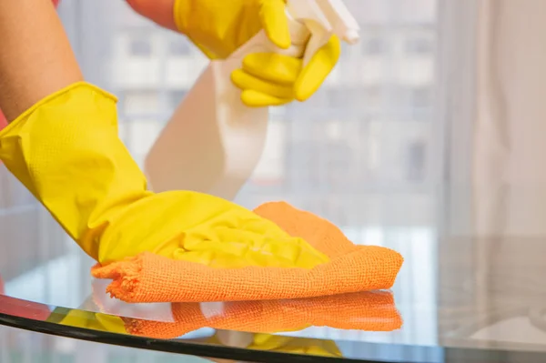Frau in gelben Handschuhen putzt Glastisch. — Stockfoto
