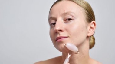 Makyajsız güzel bir kadın yeşil yüz silindiri kullanarak masaj yaptırıyor. Kadın gençleştirme masajı yapıyor.