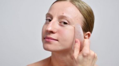 Makyajsız güzel bir kadın yeşil taşla masaj yaptırıyor. Kadın gençleştirme masajı yapıyor gua sha