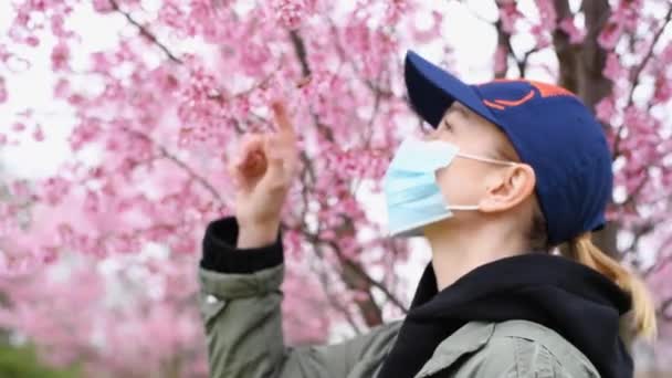 春天开始了在公园开花的树木中 戴着花粉过敏防护面罩的年轻女子 — 图库视频影像