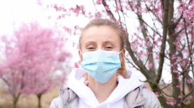 Güzel kadın tıbbi bir maske takıyor ve alerjiden sonra çiçek açan ağacın tadını çıkarıyor.