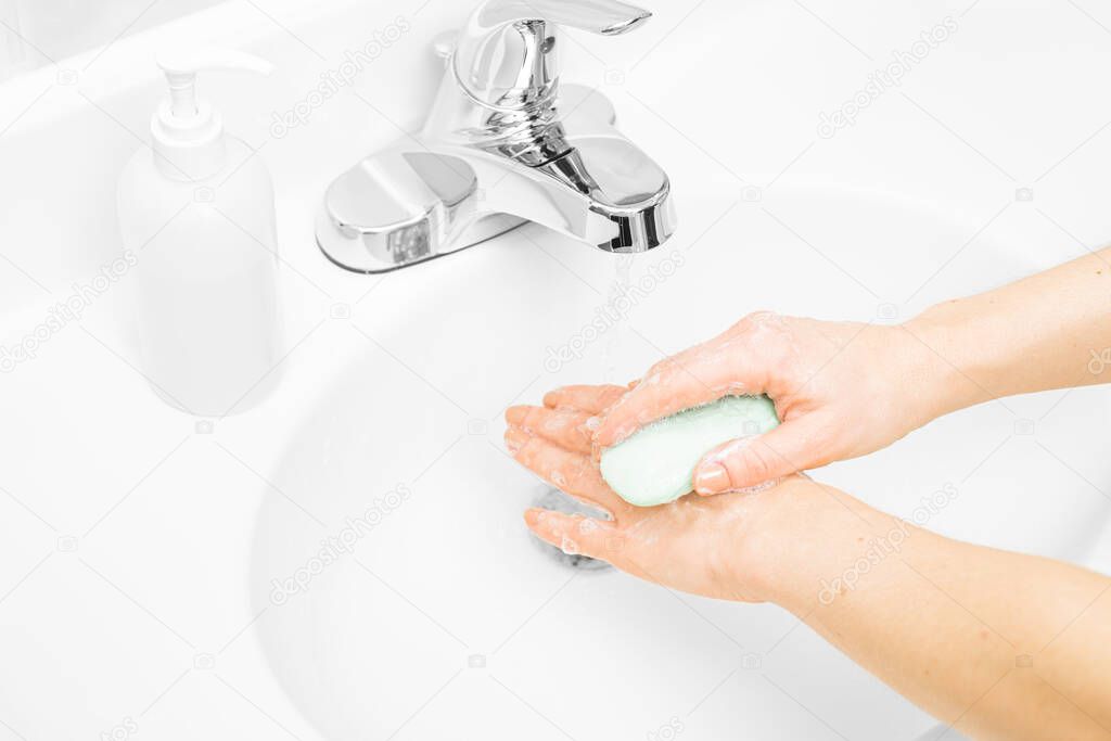 Woman washes her hands with soap under running water in sink
