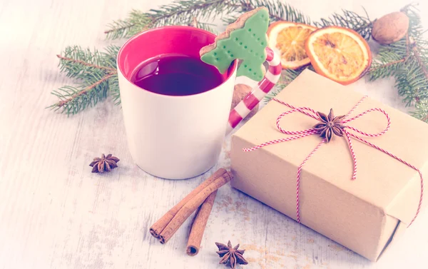 Beyaz ahşap arka plan üzerinde krema, çam, portakal dilimleri, tarçın, anason ve ceviz ile ev yapımı tereyağı fındık noel ağacı şeklinde çerez. Bir fincan dut çayı ve kraft kağıdına sarılmış bir hediye kutusu. Chri