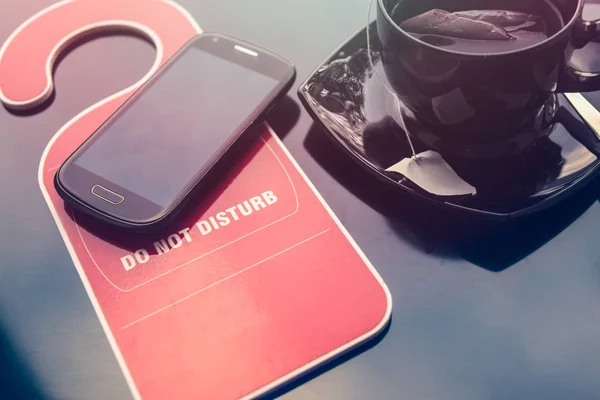 Değil disturbe işareti, bir fincan çay ve bir cep telefonu üzerinde koyu arka plan yapmak. Zaman dinlenme konsepti için.