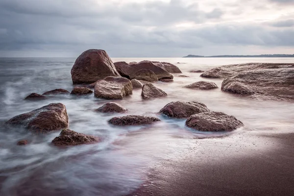 Восход солнца над морскими скалами на пляже. Гладкая вода, эффект длительного воздействия. Морской пейзаж в красивых голубых и фиолетовых цветах . — стоковое фото