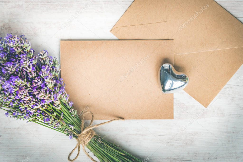 Top view of an empty greeting kraft card and envlope, lavender bouquet and silver heart over white wood rustic wooden table. Kraft mockup.