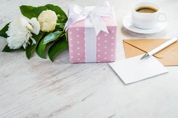 Noktalı hediye kutusu, boş tebrik kartı, kraft zarf, peonies buket ve kahve Kupası Beyaz ahşap rustik masa üzerinde pembe. Romantik tatil ve olay kavramı.