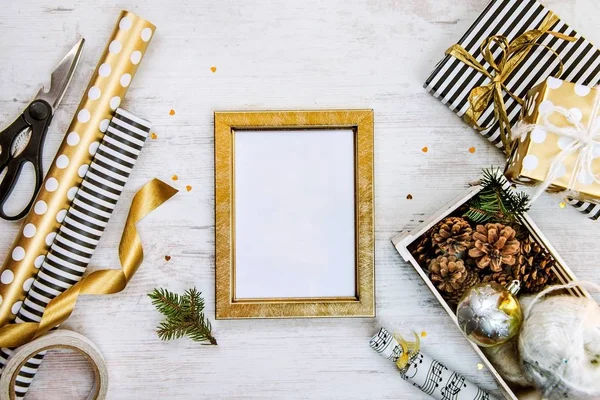 Altın ptoto çerçeve, hediye kutuları, çam kozalakları ve Noel oyuncak ve ambalaj malzemeleri bir beyaz tahta eski arka plan üzerinde dolu bir sandık. Noel kavramı. Çerçeve kadar sahte.