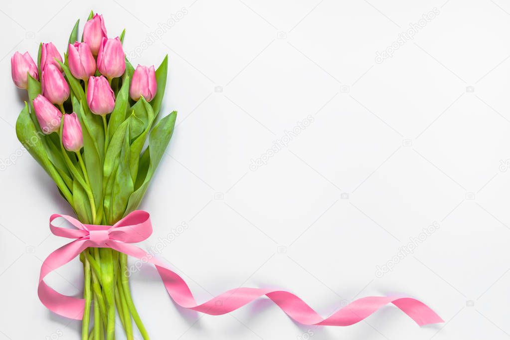 Top view of pink tulips bouquet, wrapped with pink ribbon over white background. Copy space.