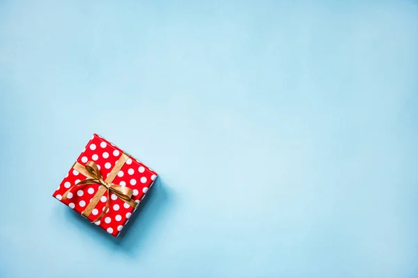 Vista superior de una caja de regalo punteada roja atada con lazo dorado sobre fondo azul. Copiar espacio . — Foto de Stock