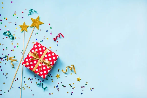 Vista superior de una caja de regalo con puntos rojos, varitas mágicas doradas, confeti colorido y cintas sobre fondo azul. Concepto de celebración. Copiar espacio . — Foto de Stock