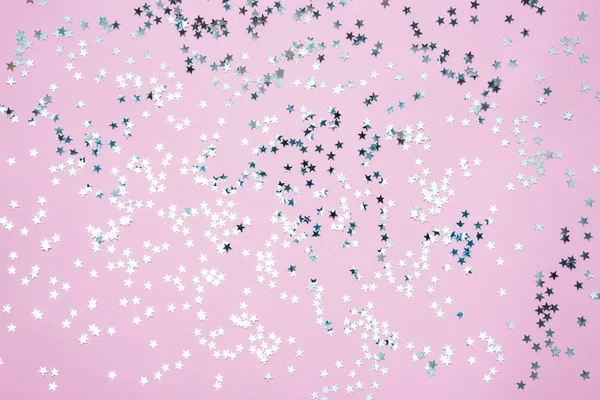 Lentejuelas plateadas en forma de estrella sobre fondo rosa . — Foto de Stock