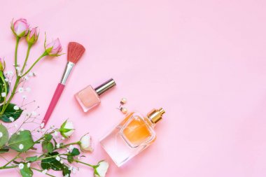 Flat lay of female cosmetics products and accessories. A bottle of perfume, nude nail polish, pearl earings and roses over pink background. Copy space. clipart