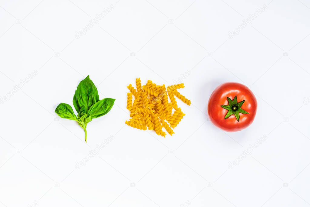 Top view of pasta ingredients over white background - raw fusilli, fresh basil and ripe tomatoe. Italian food concept.