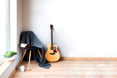 Çağdaş iç mimari. Beyaz bir duvarın önünde yün gri battaniye ve akustik gitarla kaplı siyah sandalye. Hobi ve kiralama zamanı..