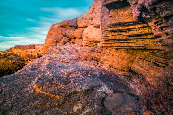 Sandstrandfelsen, orange gefärbt unter den Strahlen der aufgehenden Sonne. — Stockfoto