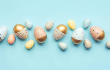 Altın renkli ve farklı renklerde Paskalya yumurtalarının üst görüntüsü. Mavi arka plan. Boşluğu kopyala.