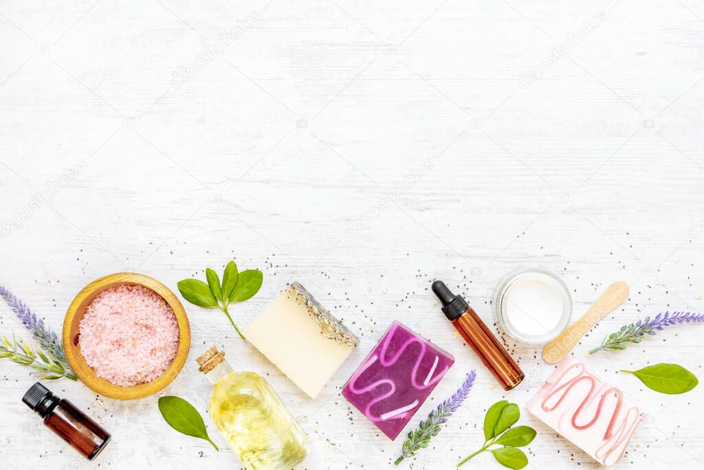 Top view of organic soaps and cosmetics arranged with lavender, herbs, chia seeds and essential oils. White rustic background, copy space.