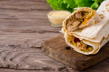 Shawarma tavuk rulo bir pide taze sebze ve krema sos ile ahşap arka plan üzerinde. Seçici odak
