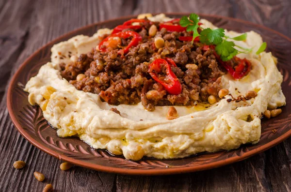 Hummus cremoso con carne picante de cordero picada en tazón de barro sobre fondo de madera. Comida Ramadán . — Foto de Stock