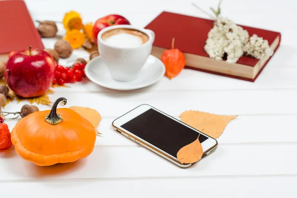 Fondo de otoño, taza de capuchino, teléfono móvil sobre mesa de madera . — Foto de Stock