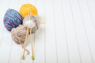 Örgü iplik topları ve iğneler Beyaz ahşap zemin üzerinde.