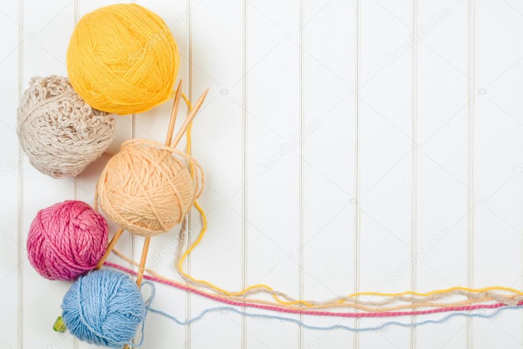 Knitting yarn balls and needles on white wooden background.