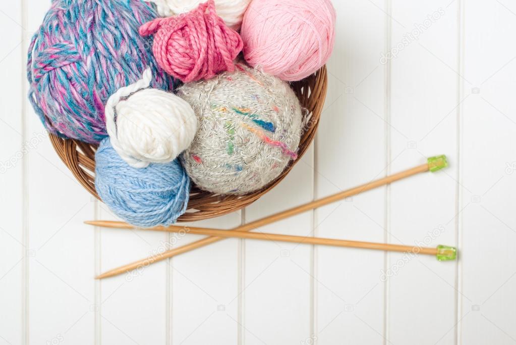 Knitting yarn balls and needles on white wooden background.