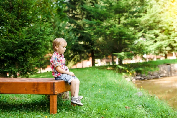 微笑的快乐的男孩，坐在长椅上湖附近。夏季时间周末心情. — 图库照片